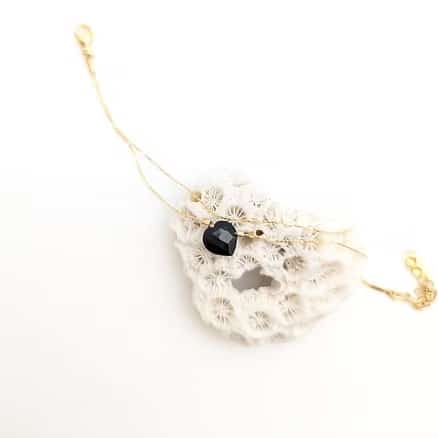 Bracelet double chaîne délicat en or avec pendentif cœur noir facetté et petites perles, présenté sur un fragment de corail blanc.