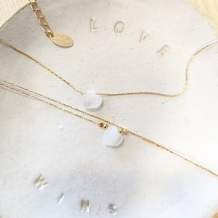 Deux colliers chaîne en or avec des pendentifs cœur blancs délicats posés sur une coupelle gravée "LOVE WINS". Bijoux élégants.