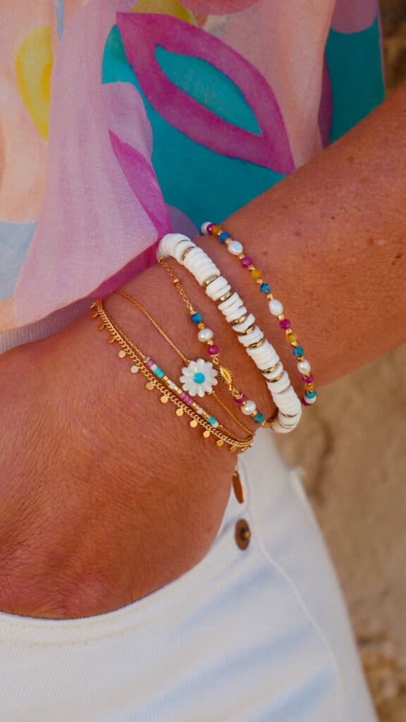 Bracelets Colorés et Dorés Style Bohème Chic pour Femme Main portant plusieurs bracelets colorés et dorés de style bohème, dont un avec une fleur de marguerite blanche.